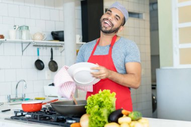 Handsome hispanic kitchen assistant cleaning plates at work at restaurant