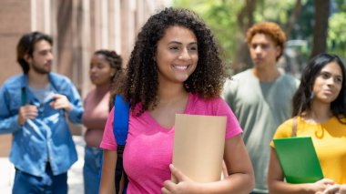 Pretty latin american female student with group of caucasian and african american young adults outdoor in city