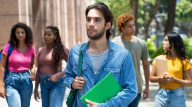Handsome latin american male student with group of caucasian and african american young adults outdoor in city