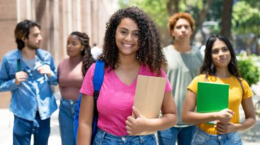 Laughing latin american female student with group of caucasian and african american young adults outdoor in city