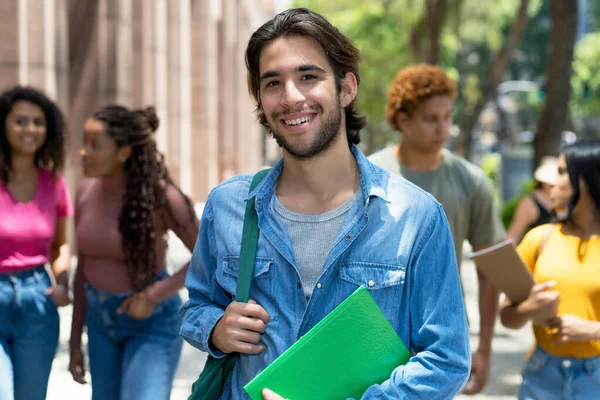 Laughing latin american male student with group of caucasian and african american young adults outdoor in city