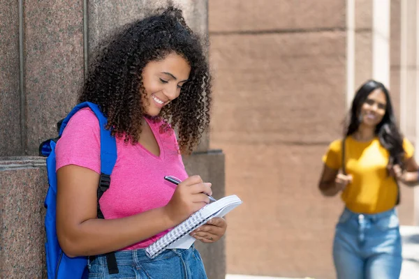 メキシコ人の女子学生が市内の大学ビルの前でメモを書いて笑っています — ストック写真