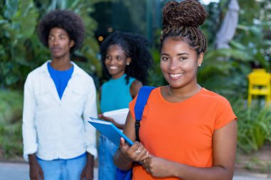 Pretty african american female student with group of black young adults outdoors in summer clipart