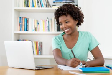 Afrika kökenli Amerikalı kız öğrenci üniversite kütüphanesinde mezuniyet için hazırlanıyor.