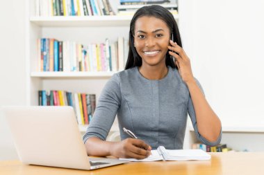 Latin Amerikalı iş kadını müşterisiyle şirket ofisinde telefonda konuşuyor.