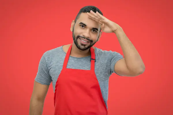 Laughing hispanic waiter with apron on red background for cut out looking for guests