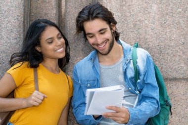 Latin Amerikalı erkek öğrenci ve Meksikalı kız öğrenci gülerek sınav için şehir dışına çıkıyorlar.