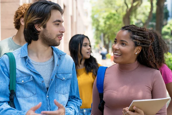 Latin american male student talking with black female student about graduation outdoor in city in summer