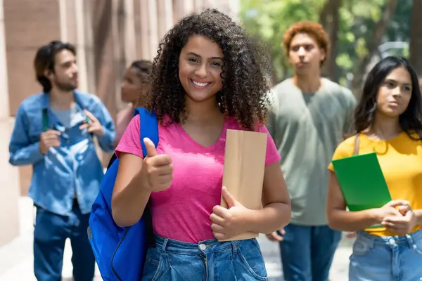Latin american female student showing thumb up with group of caucasian and african american young adults outdoor in city
