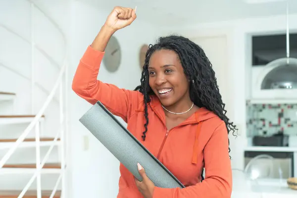 Excited black woman with yoga mat ready for class at gym indoors at home