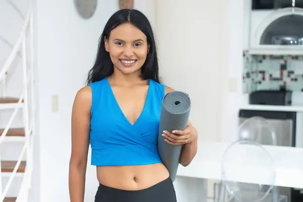 Beautiful latin american woman with yoga mat ready for class at gym indoors at home