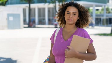 Sırt çantası ve evrak işleri olan İspanyol kız öğrenci yazın şehir dışında üniversitenin önünde.