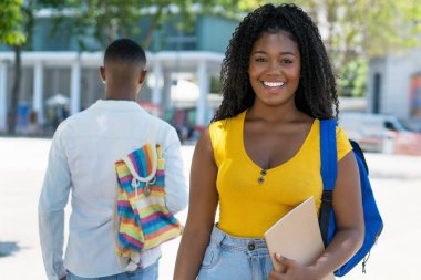 Sırt çantalı siyah kız öğrenci ve arka planda erkek öğrenci.