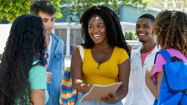 Lachende Afrikanisch Amerikanische Studentin Gespräch Mit Einer Gruppe Hispanischer Und lizenzfreie Stockfotos