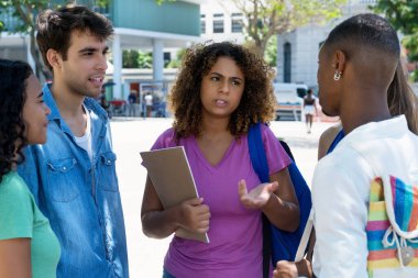 Pretty latin american female student in discussion with caucasian and hispanic and black young adults outdoor in summer in city