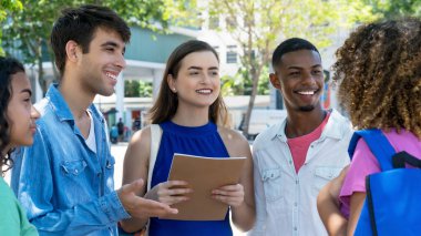German female student talking with hispanic and latin american and black young adults outdoor in summer in city