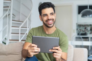 Evde tablet bilgisayarlı şık sakallı Latin Amerikalı adam internetten alışveriş yapıyor.