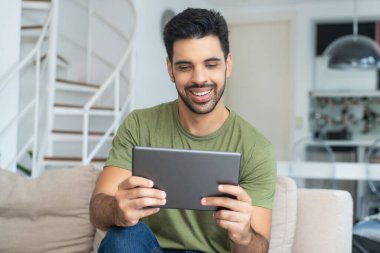 Evdeki tablet bilgisayarında modaya uygun sakallı Latin Amerikalı bir adam film yayınlıyor.