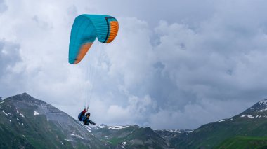 Tiflis, Gürcistan-Haziran 06.2024: Kazbegi dağları arasında yamaç paraşütü yapan insanlar.