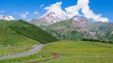 Kazbek dağlarındaki çimenli tepeden panoramik manzara ve yeşil vadi yollarla kesişiyor.