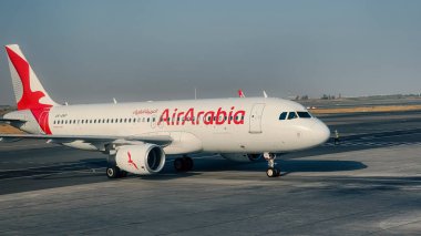Doha, Katar, 12 Ekim 2024: Sharjah Havaalanı, BAE 'de Air Arabia uçağı yolcu alımı ve havayolunun imzalı kırmızı ve beyaz üniformasıyla pistte sergilenmektedir..