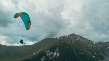 Tiflis, Gürcistan-Haziran 06.2024: Kazbegi dağları arasında yamaç paraşütü yapan insanlar.