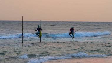 Weligama, Sri Lanka-18 Ocak 2025: Geleneksel stil balıkçıları, Sri Lanka kıyılarına özgü antik bir balıkçılık yöntemi uygulayarak, dalgaların üzerindeki tahta direklere tünediler..