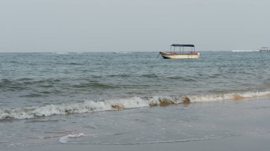 Hikkaduwa, Sri Lanka - 18 Ocak 2025: Sri Lanka kıyı şeridinin doğal güzelliğini gözler önüne seren, altın kumları, turkuaz suları ve berrak mavi gökyüzü altında hafif dalgaları olan sakin bir sahil manzarası.