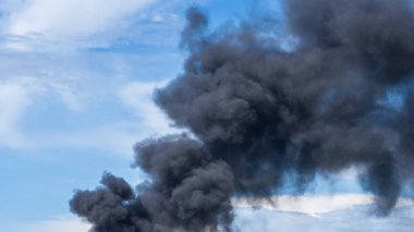 Alevli bir ateşten yükselen kalın siyah duman, gün ışığı altında dramatik ve yoğun bir sahne yaratıyor..