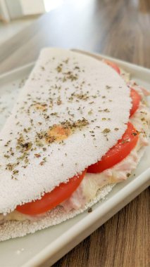 Kare beyaz tabakta peynirli ve jambonlu Brezilya Tapyokası.