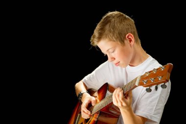 Happy boy playing on acoustic guitar. Teenager boy with classic wooden guitar. boy learning to play guitar on black background. Music education and extracurricular lessons.