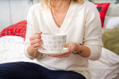 Beyaz kazaklı bir kız elinde bir fincan sıcak kahve ya da bir Noel ağacının arka planında çay tutuyor. Sıcak Noel atmosferi. Noel için alkolsüz sıcak bir içki. Yaşam biçimi