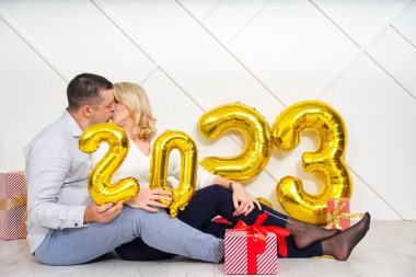 2023 altın folyo şişirilebilir balonlarla Noel arifesinde romantik bir randevuya çıkan genç çift. Noel ve 2023 Yeni Yıl Tatili konsepti.