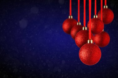 Kırmızı Noel ağacı süslemeleri fotokopi alanından sarkıyor. Soyut koyu mavi arka planda asılı duran cam veya plastikten yapılmış Noel topları.