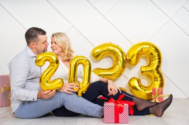 2023 altın folyo şişirilebilir balonlarla Noel arifesinde romantik bir randevuya çıkan genç çift. Noel ve 2023 Yeni Yıl Tatili konsepti.