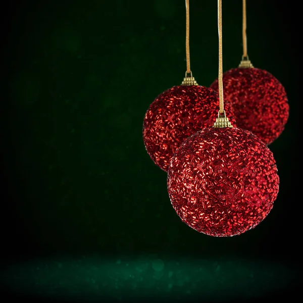 Red Christmas tree ornaments hanging with copy space. Christmas Balls made of glass or plastic hanging over abstract dark green background.