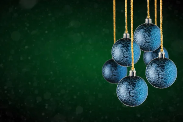 Blue Christmas tree ornaments hanging with copy space. Christmas Balls made of glass or plastic hanging over abstract dark green background.