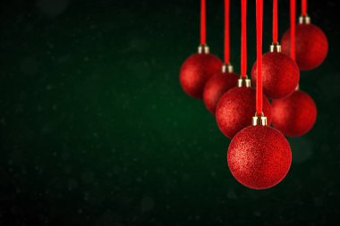Kırmızı Noel ağacı süslemeleri fotokopi alanından sarkıyor. Soyut koyu yeşil arka planda asılı cam veya plastikten yapılmış Noel topları.