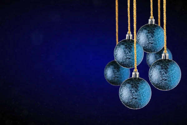 Blue Christmas tree ornaments hanging with copy space. Christmas Balls made of glass or plastic hanging over abstract dark blue background.
