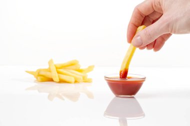 Beyaz arka planda gölgeli ketçapa el daldırılmış patates cipsi cipsi.