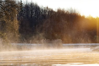 Nordic landscape at sunrise time. Early morning after a cold night, fog forms from the warm wetland in nature and the sun lights up and gives different colors.