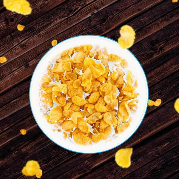 Bowl of sweet cornflakes with milk dark wooden table background, top view. Corn flakes with milk splashes dark wooden table