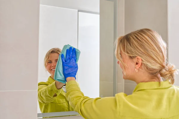 cleaning company. hotel maid microfiber cloth washing cleaning a mirror. household service concept. woman cleaning mirror in bathroom