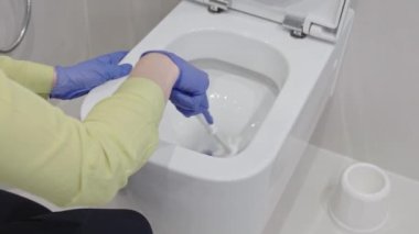 Deterjanla duvar monte edilmiş tuvalet temizliği. Kadın otel hizmetçisi banyo tuvaletini fırçayla temizliyor. Ev servisi. Modern sifon tuvaleti. Temizlik