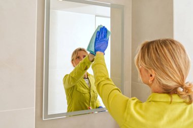 cleaning company. hotel maid microfiber cloth washing cleaning a mirror. household service concept. woman cleaning mirror in bathroom