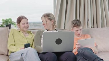 Happy family with kids sit on sofa in living room have fun using laptop together, smiling parents rest on couch enjoy weekend with childrens laugh watch video on computer at home