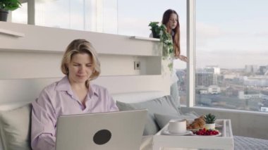 Happy middle aged, beautiful woman having breakfast, relaxing in hotel bed. Woman having breakfast sitting on her bed in luxury apartments. enjoying lazy morning lifestyle
