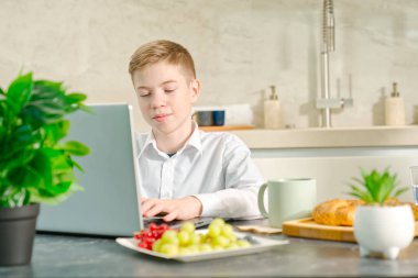 young boy, teenager plays on the notebook during breakfast time. Addiction to gadgets. Breakfast before school in the kitchen.