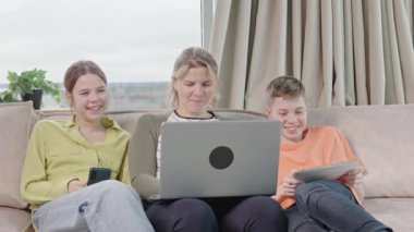 Happy family with kids sit on sofa in living room have fun using laptop together, smiling parents rest on couch enjoy weekend with childrens laugh watch video on computer at home