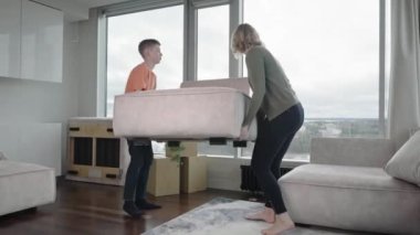 family rearranging furniture. Happy couple moving furniture in new apartment. Moving day, happy buyers. Positive smiling young couple moving furniture